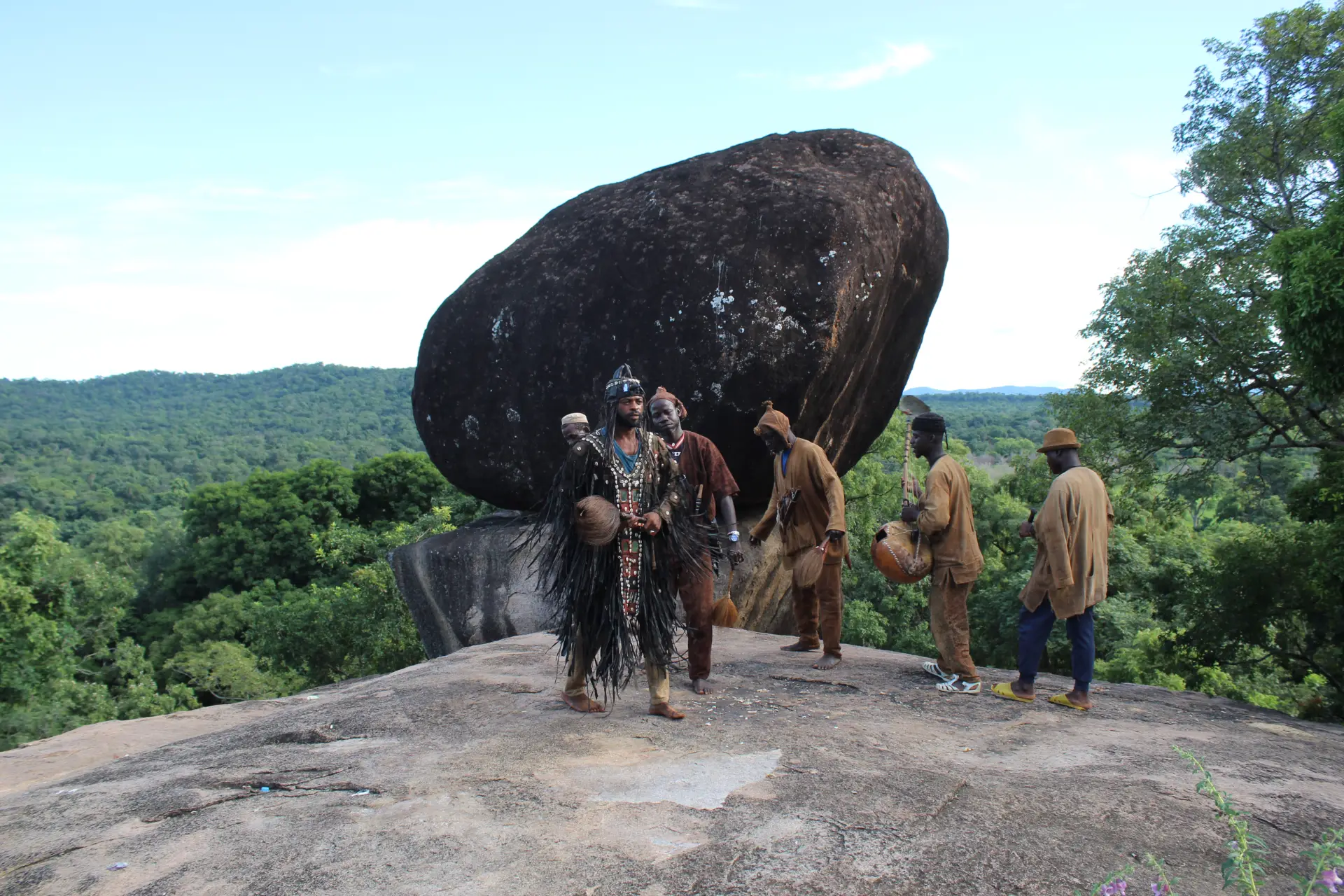Traditional performers standing beside a giant balancing rock in Ivory Coast